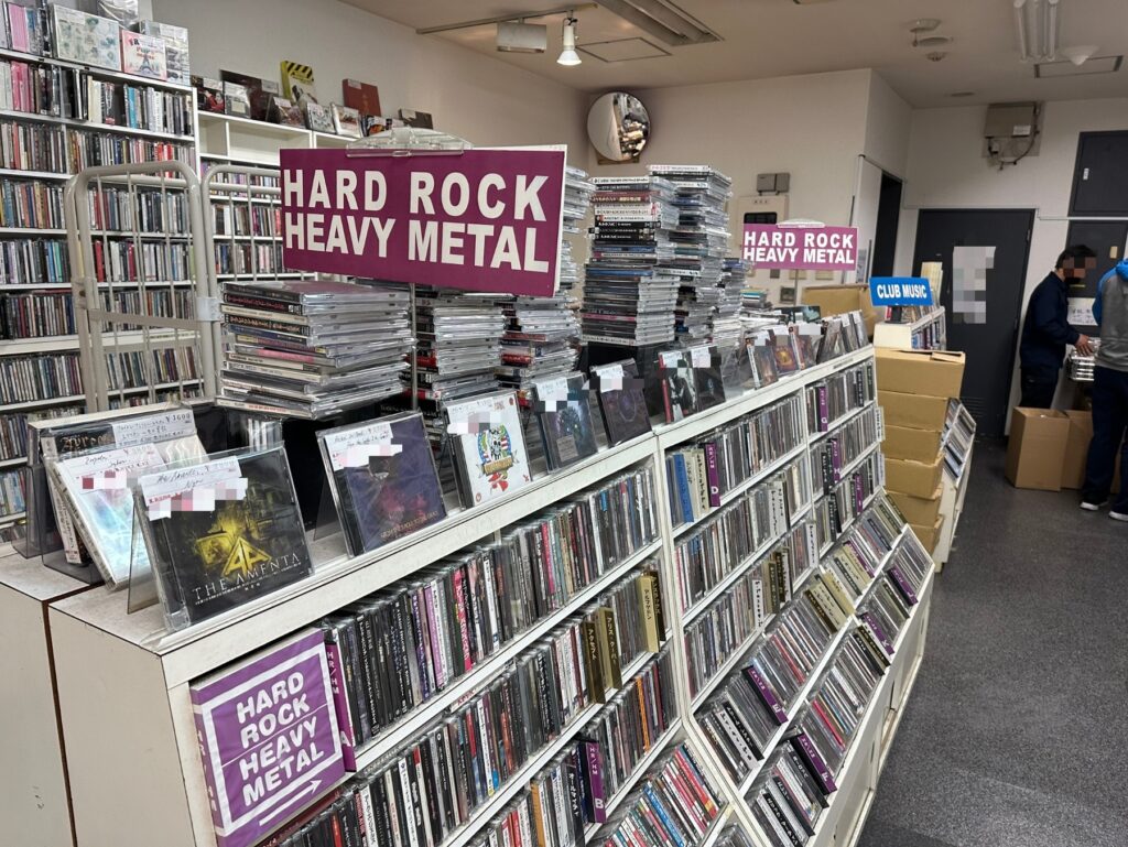ハードロック・ヘヴィメタルのCDが並ぶレコード店の店内。大量の在庫と梱包箱が見える